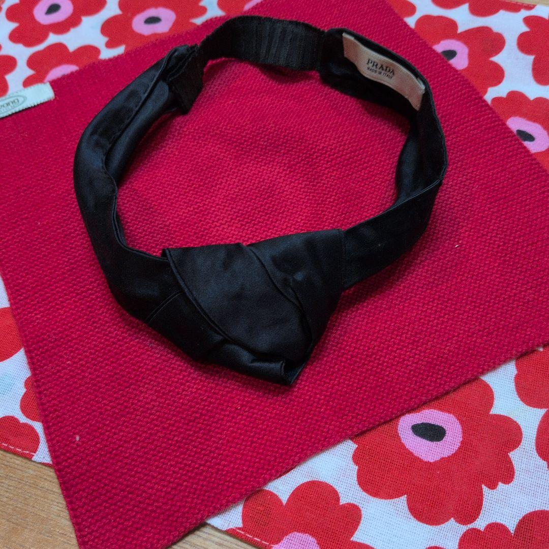 Black PRADA hair band laid flat on a red floral-patterned cloth.