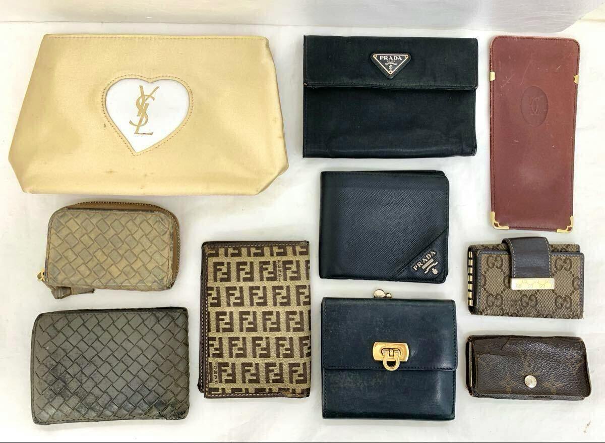 Top-down photo of ten wallets and small leather goods on a white background, including a black Prada wallet with a triangular logo.