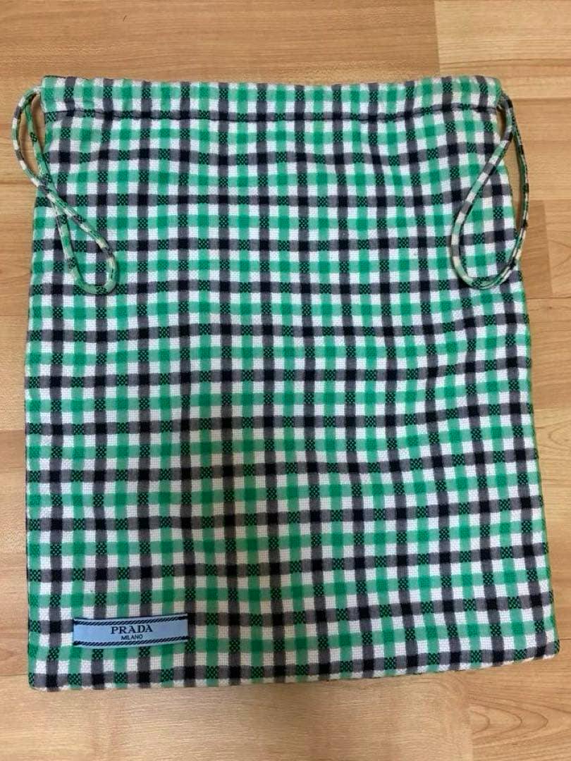 Green, black, and white checked PRADA drawstring pouch with a visible PRADA MILANO label laid flat on a wooden surface.