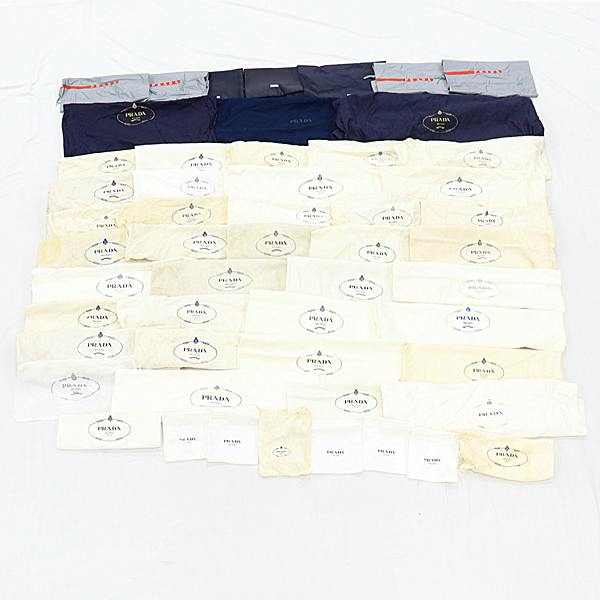 Multiple Prada dust bags laid out in rows on a white surface.