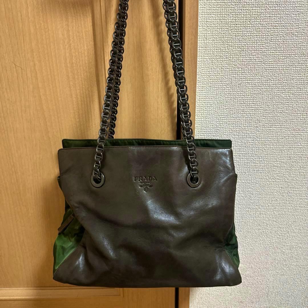 PRADA nylon dark brown shoulder bag with chain straps shown from the front, hanging against a door.