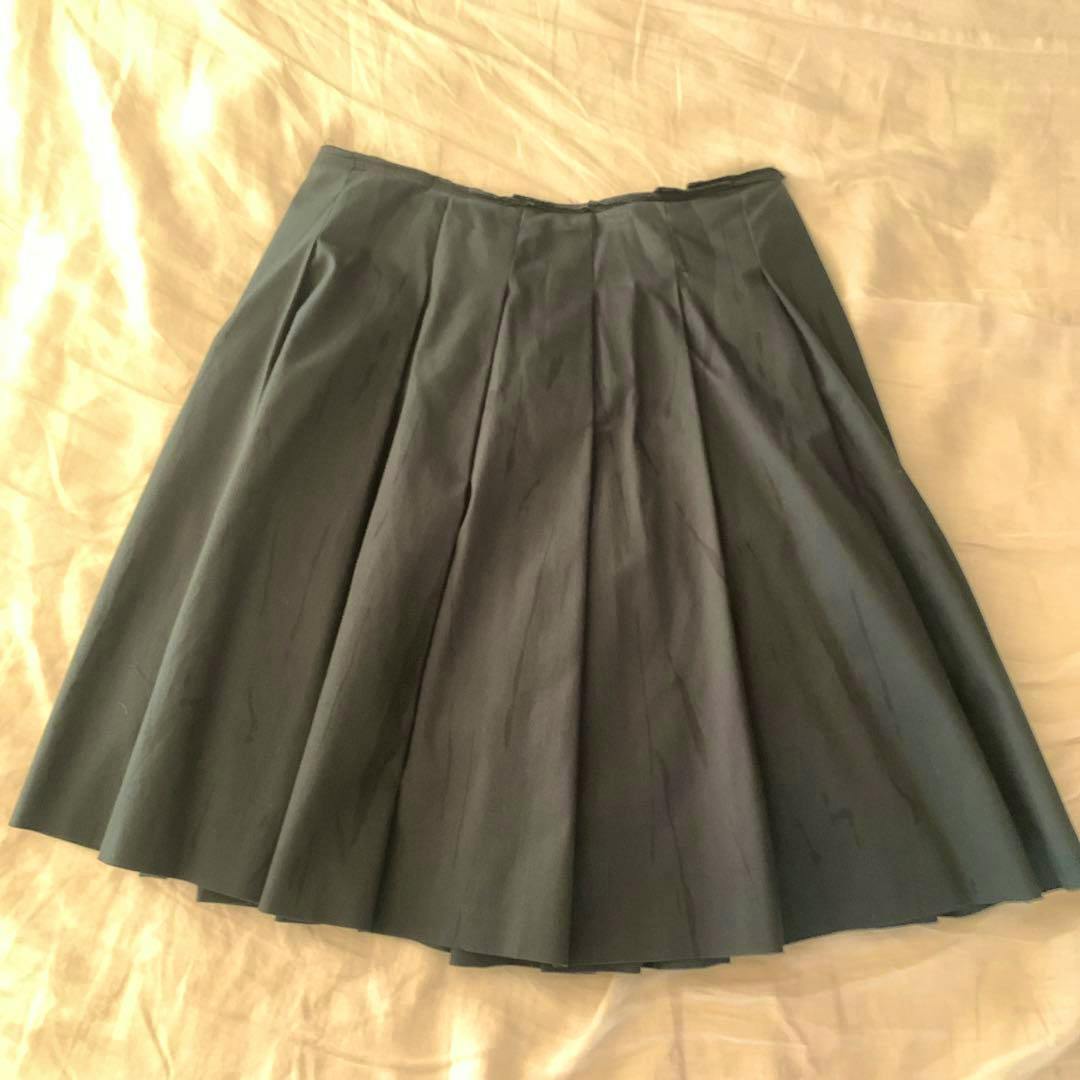 Full view of a deep green pleated flared skirt laid flat on a beige surface.