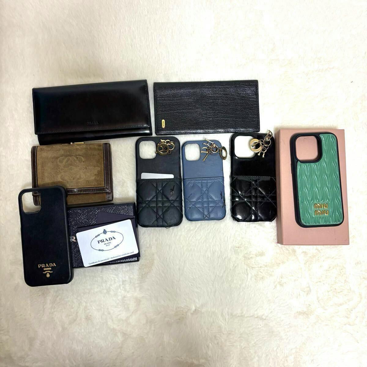 Multiple wallets and smartphone cases, including a boxed green Miu Miu phone case, laid out on a light fabric background.