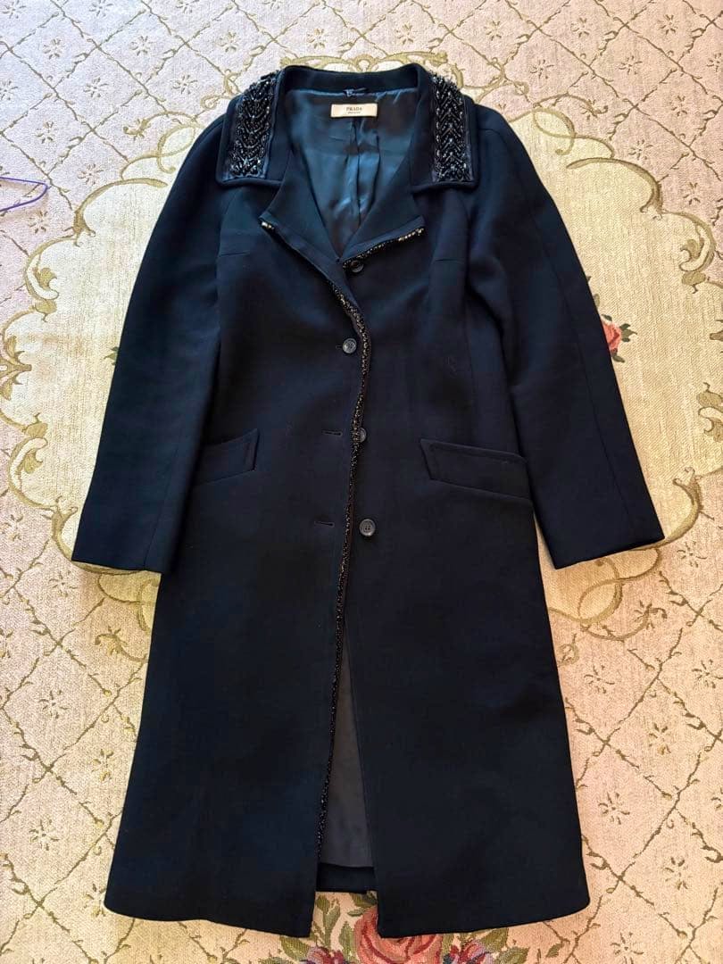 Black PRADA long coat laid flat showing the front, button closure, and embellished collar.