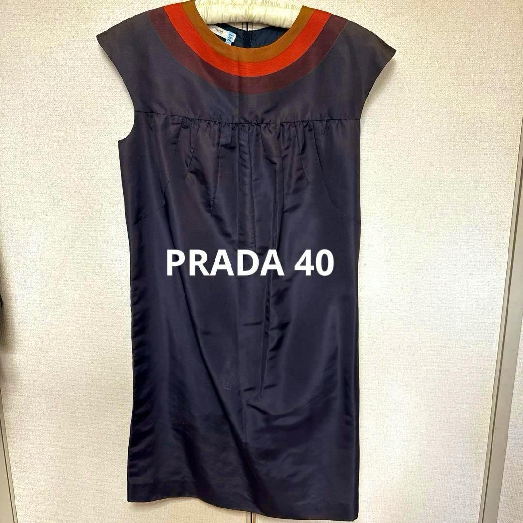 Front view of a dark blue PRADA French-sleeve dress with concentric orange, red, and brown neckline bands hanging on a hanger.