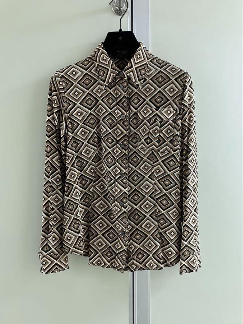 Front view of a brown geometric-print silk women's blouse hanging on a black hanger against a light background.