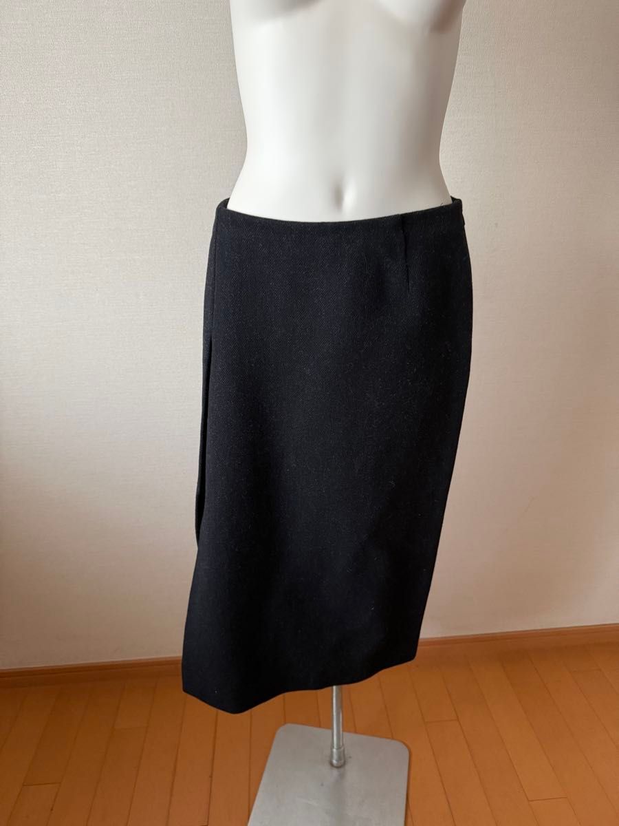 Black wool women's skirt displayed on a mannequin against a plain wall and wooden floor.