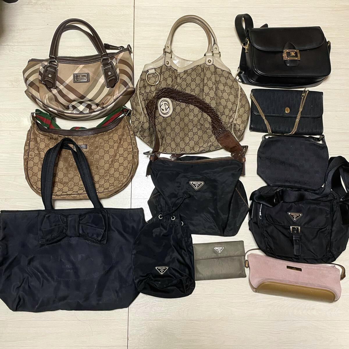 Multiple high-brand bags (Prada, Gucci, etc.) and canvas bags laid flat on a light floor as a mixed lot.
