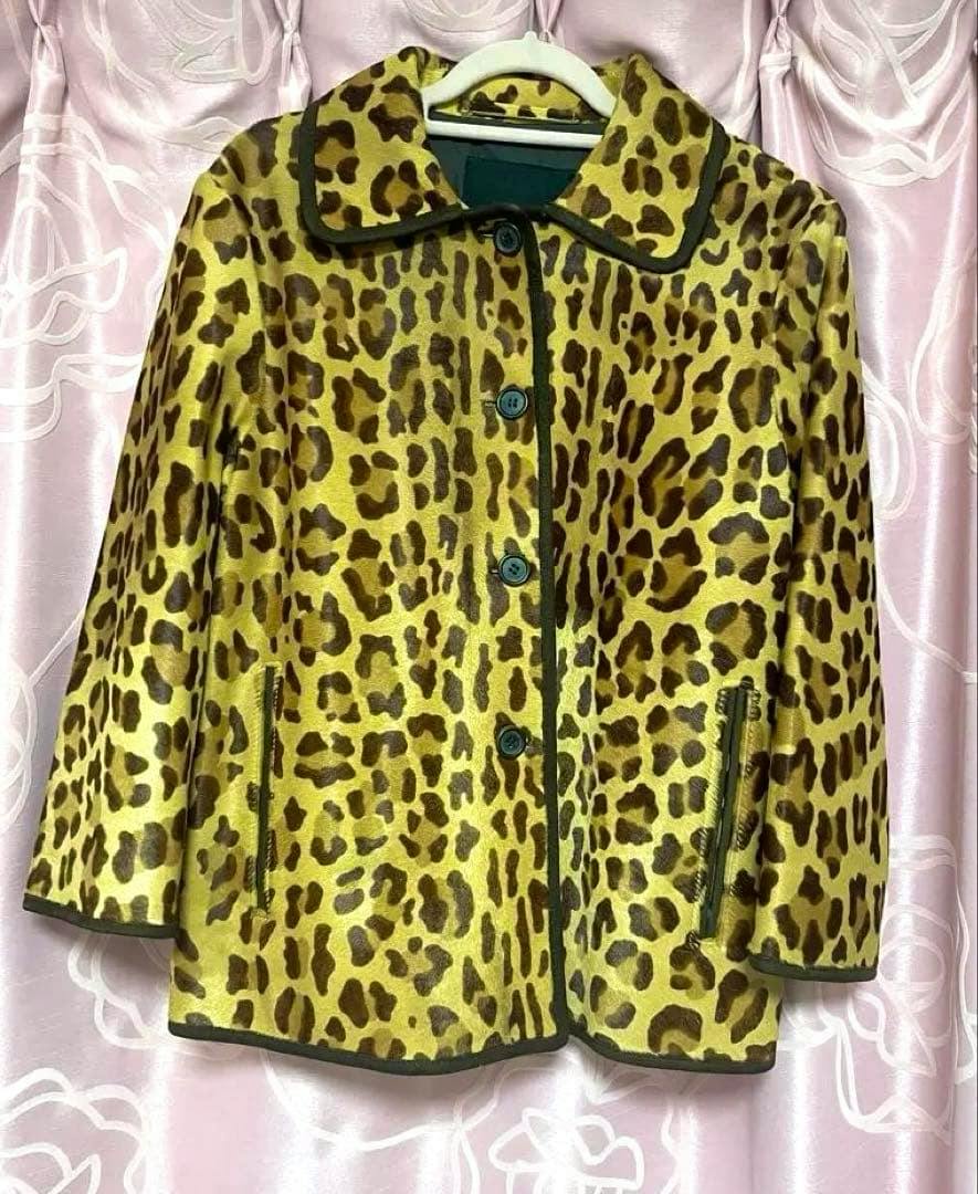 Front view of a PRADA leopard-print fur coat (mens jacket) with buttons and zippered pockets hanging on a hanger against a pink curtain.