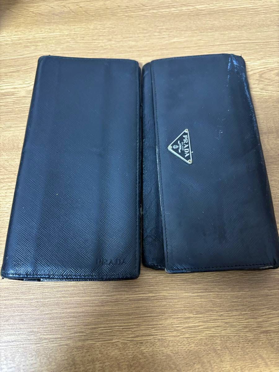 Two black long Prada wallets placed side by side on a wooden surface.