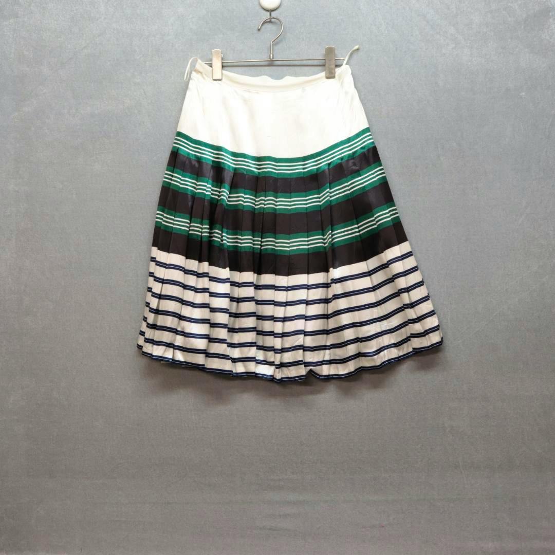 White pleated skirt with green and black horizontal stripe bands hanging on a hanger against a gray background.
