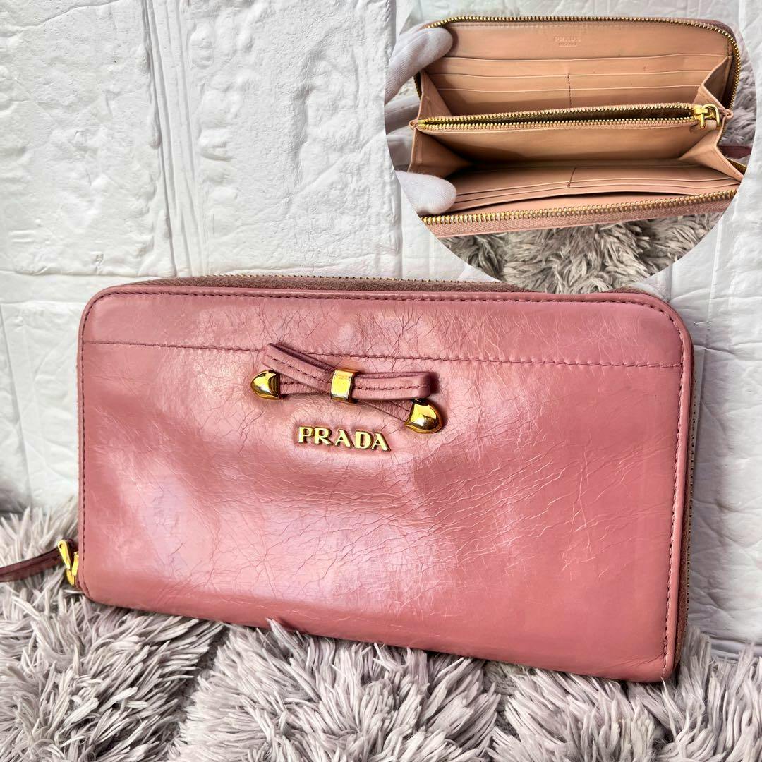 Pink PRADA round-zip leather wallet with a mini ribbon and gold metal PRADA logo, shown with an inset image of the open interior and card slots.