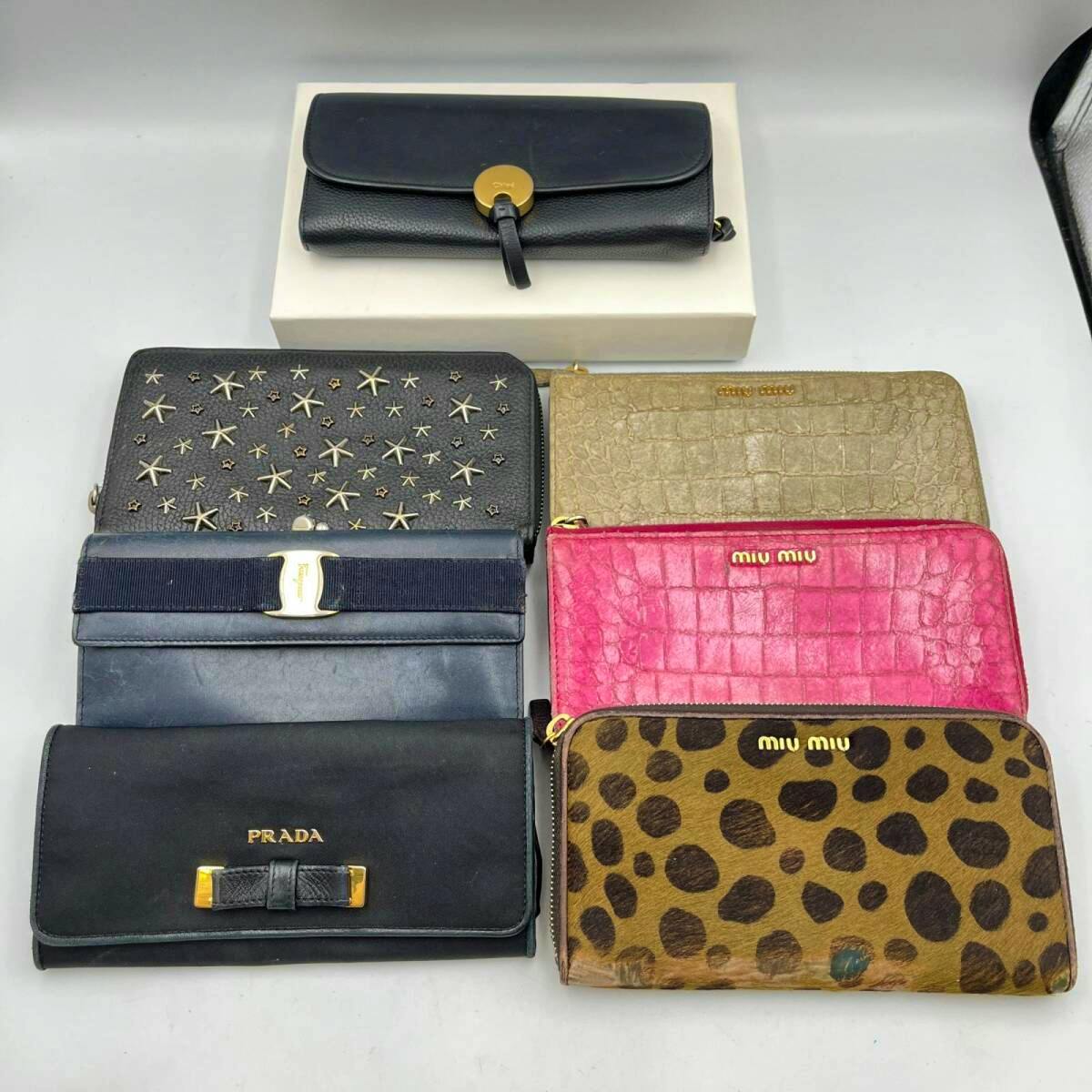 Seven long wallets in different colors and patterns arranged on a white surface.