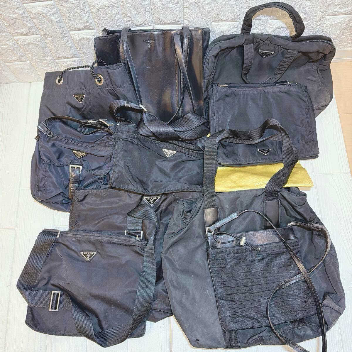 Multiple black PRADA nylon tote and shoulder bags laid out together showing triangular logo plates and straps.