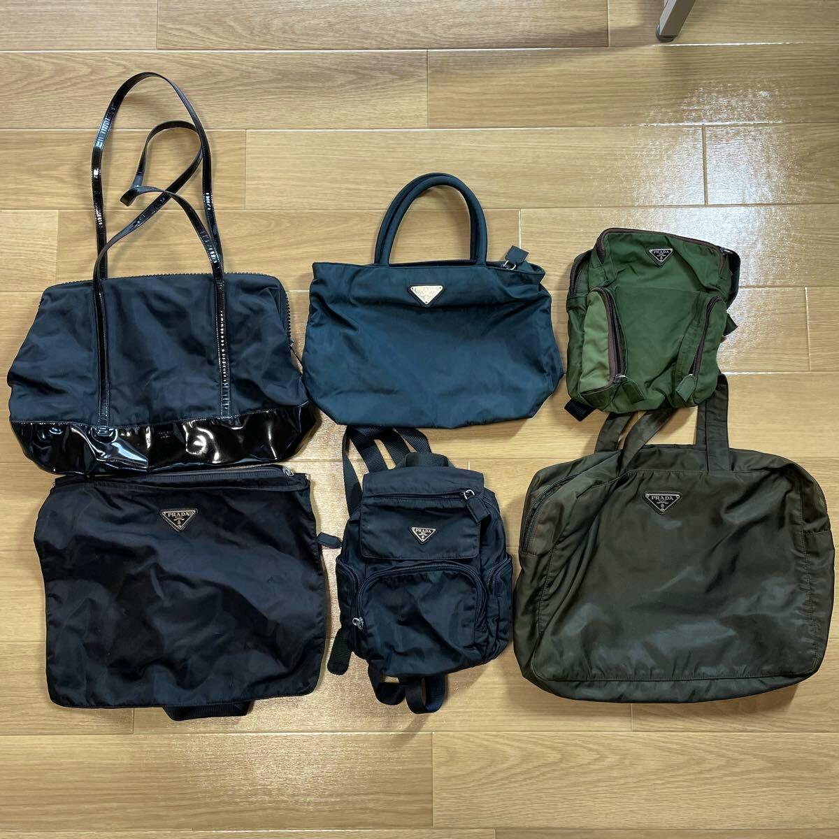 Six Prada nylon bags with triangular logos (totes, shoulder bags, backpacks) laid on a wooden floor.