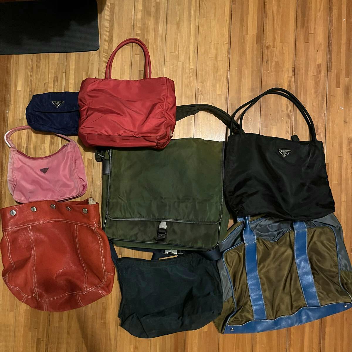 Multiple bags, including several Prada nylon handbags and pouches, arranged on a wooden floor.