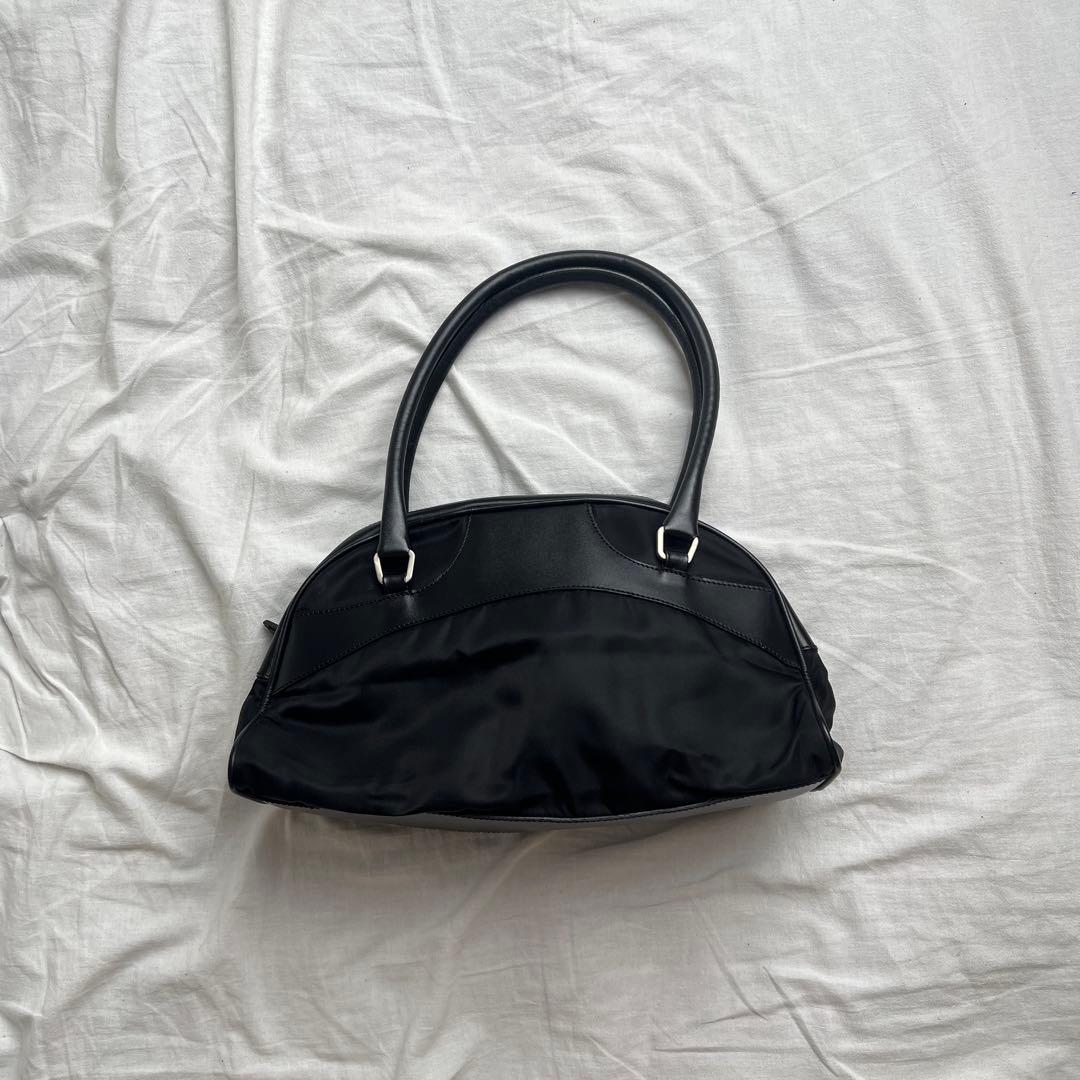 Black nylon Prada shoulder bag lying on a white sheet, shown from the front.