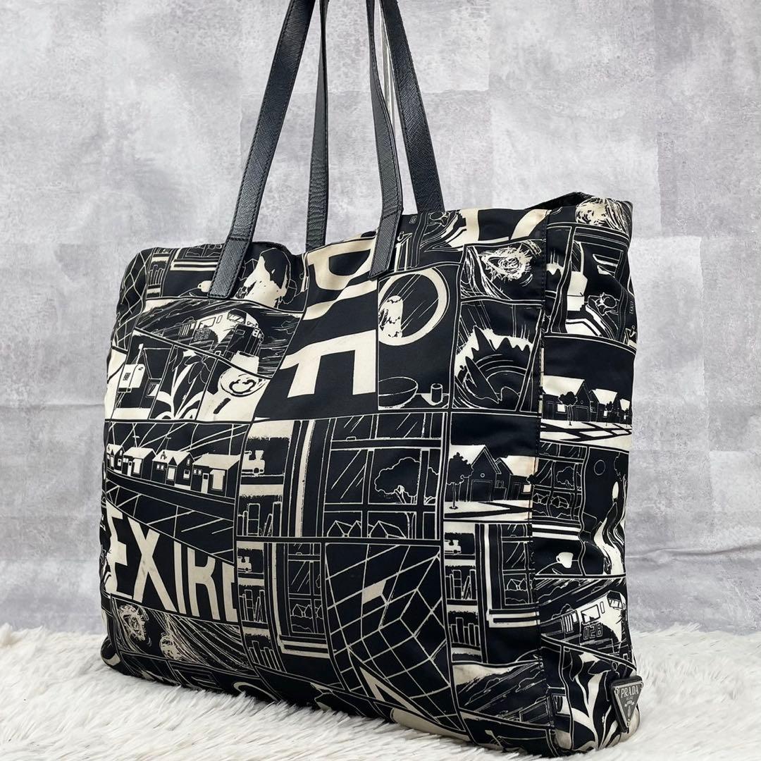 Black graphic-print Prada nylon tote bag with shoulder straps shown against a gray background.