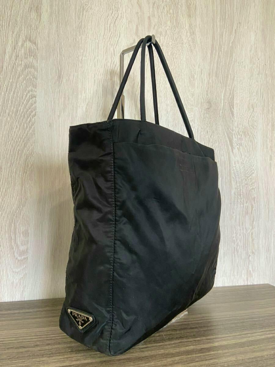 Black Prada nylon tote bag shown angled to display the side with the triangular logo plate and double handles.