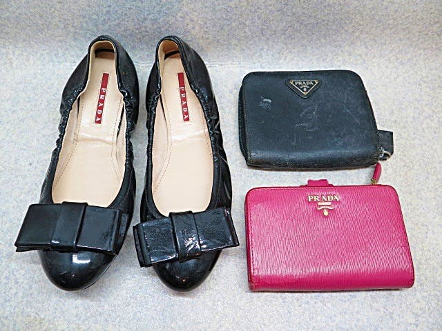 Photo of a pair of black PRADA pumps placed next to two PRADA wallets, one black and one pink.