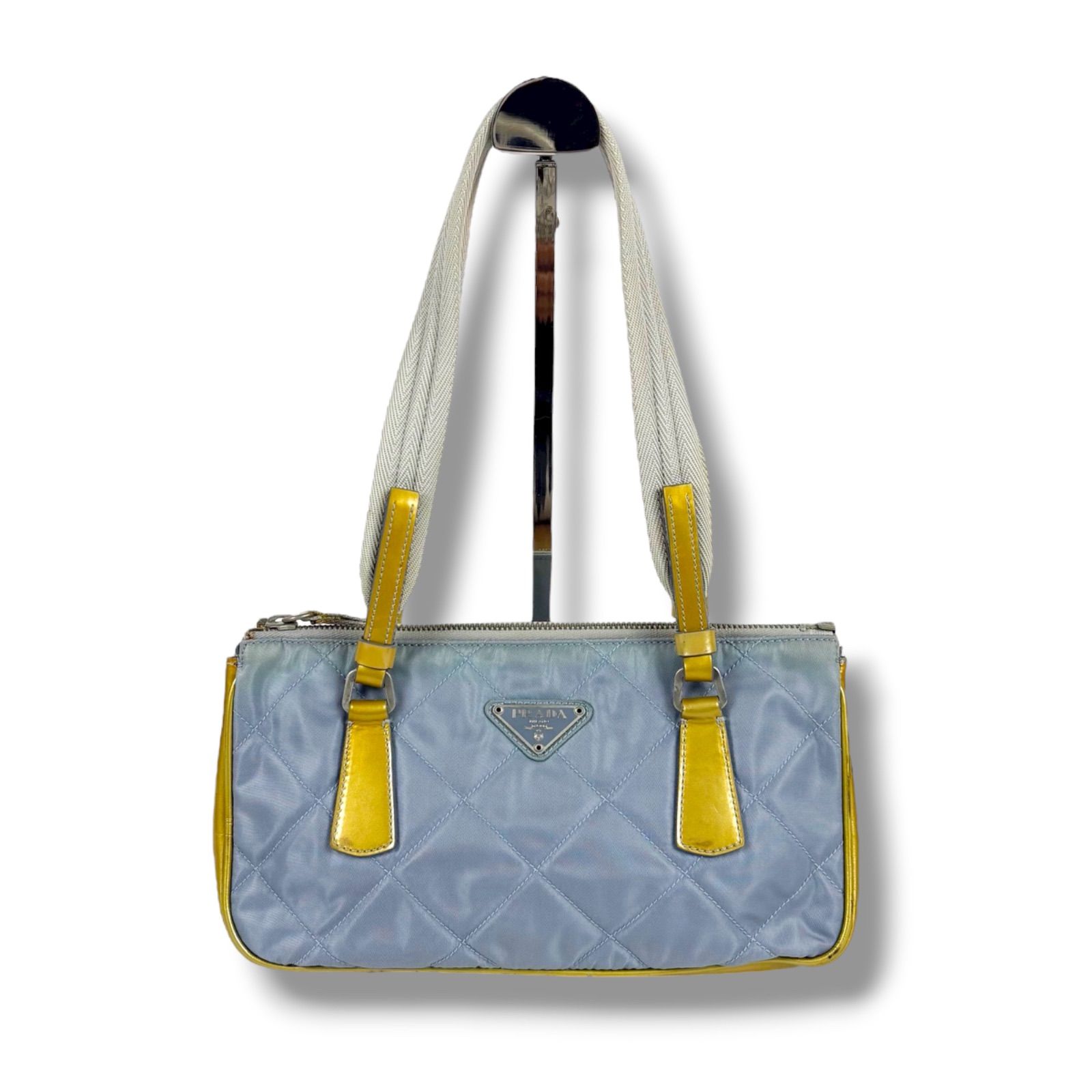 Light-blue quilted Prada mini tote bag in tessuto nylon with yellow trim, white shoulder straps, and a triangular logo plaque on the front.