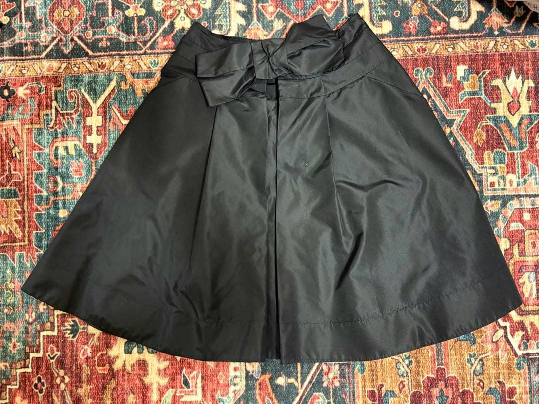 Black PRADA ribbon mini skirt (size 38) laid flat showing the front with a bow detail on a patterned rug.