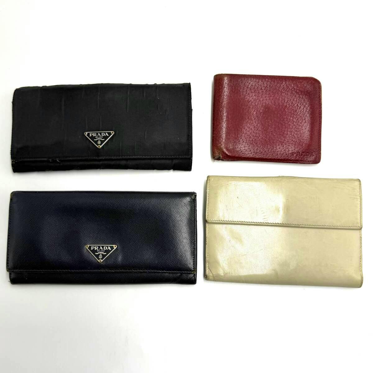 Four wallets (black, navy, red, and ivory) laid flat on a white background, two showing the PRADA triangle logo.