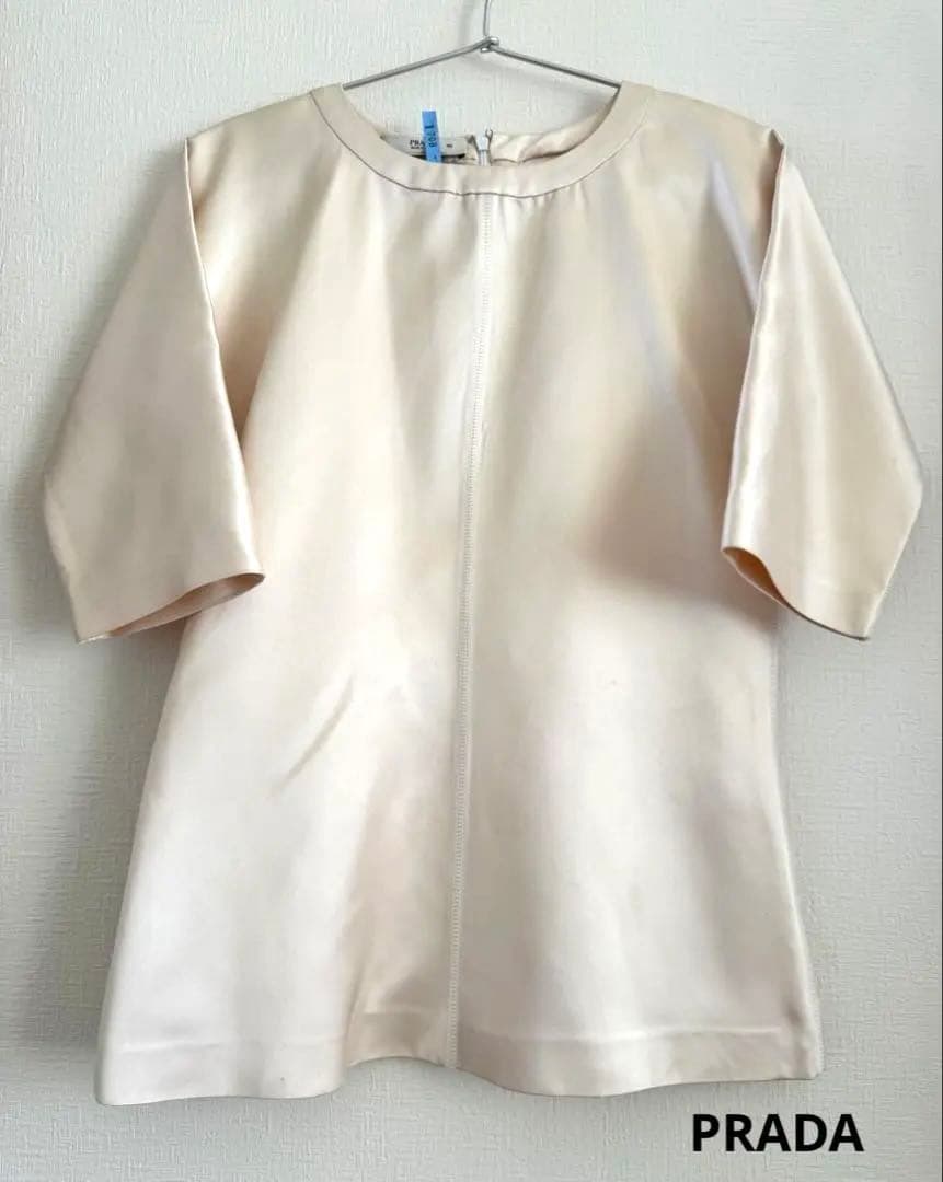 Front view of a light cream silk women's blouse hanging on a hanger.