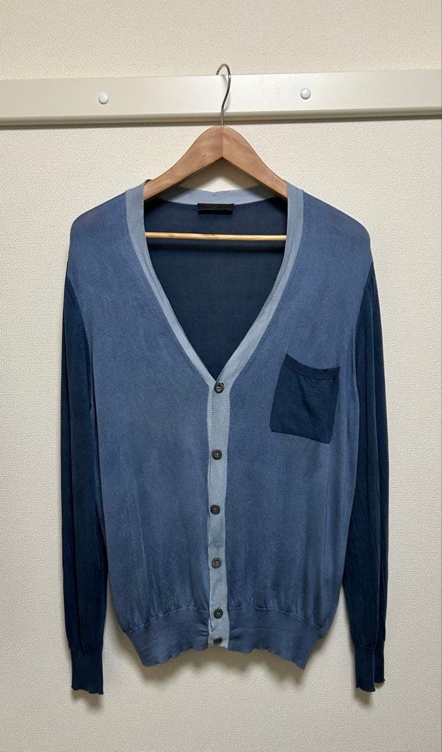 Front view of a men's Italian-made PRADA silk cardigan in blue hanging on a wooden hanger.