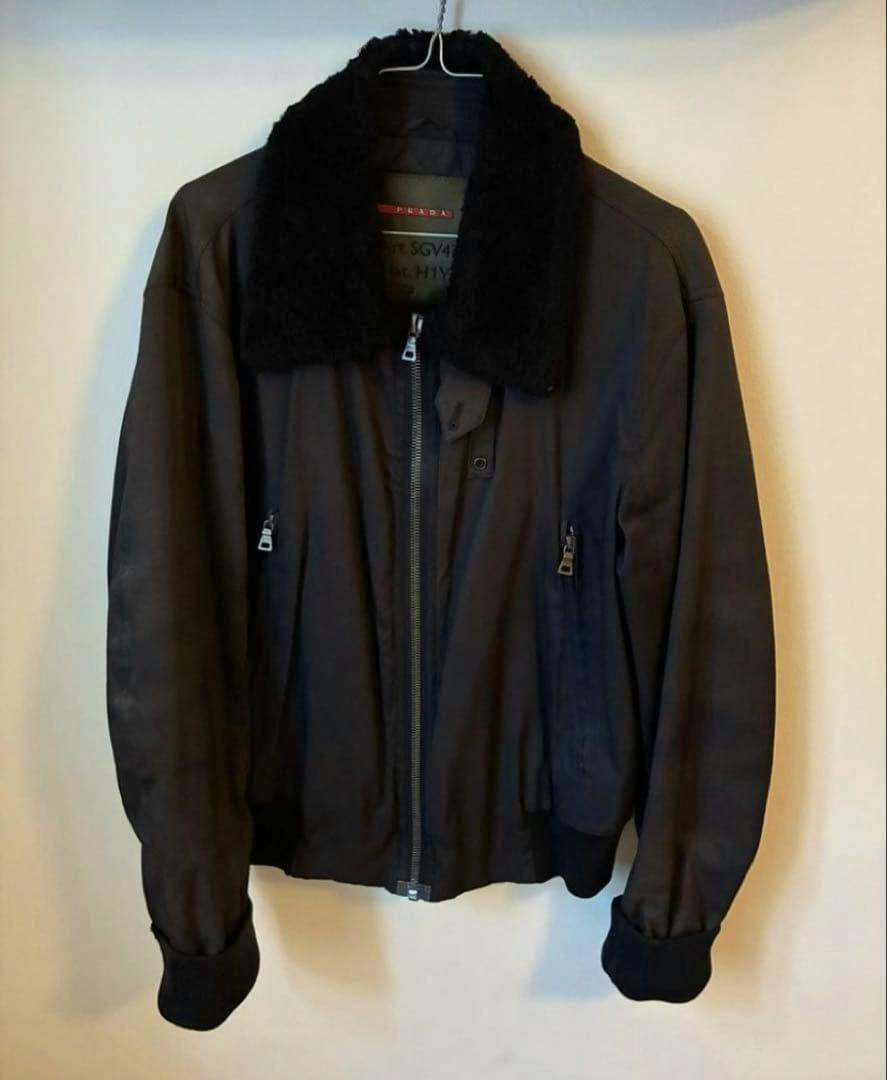 Front view of the Prada Sport men's nylon jacket with a black fur/boa collar hanging on a hanger against a plain wall.