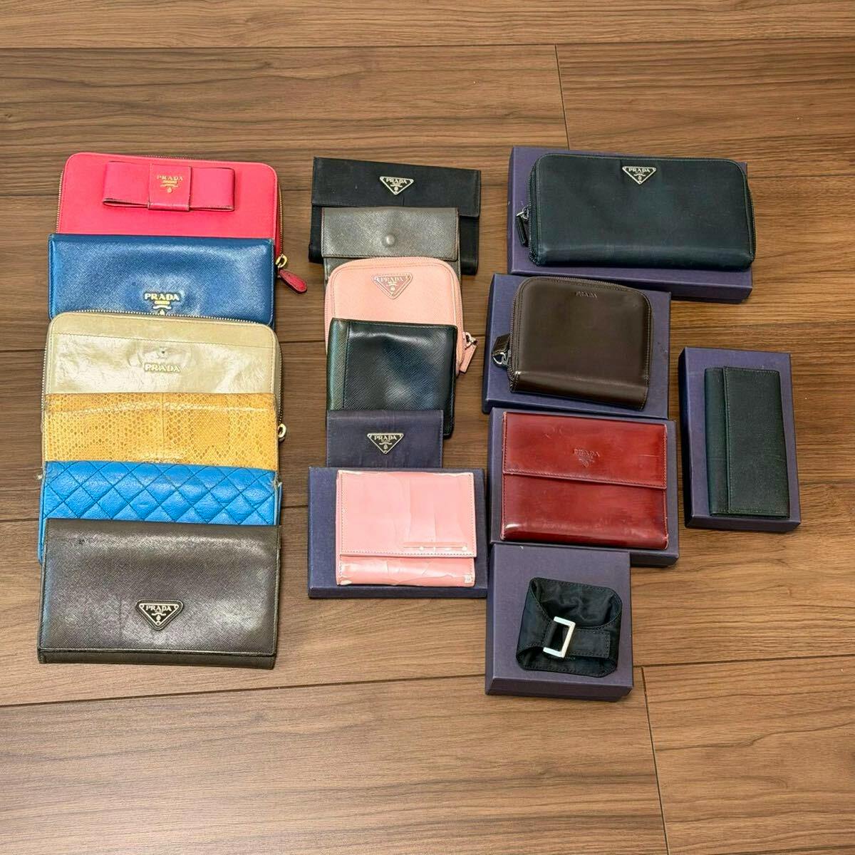 Multiple PRADA wallets and small leather goods arranged on a wooden floor, showing various colors and styles.