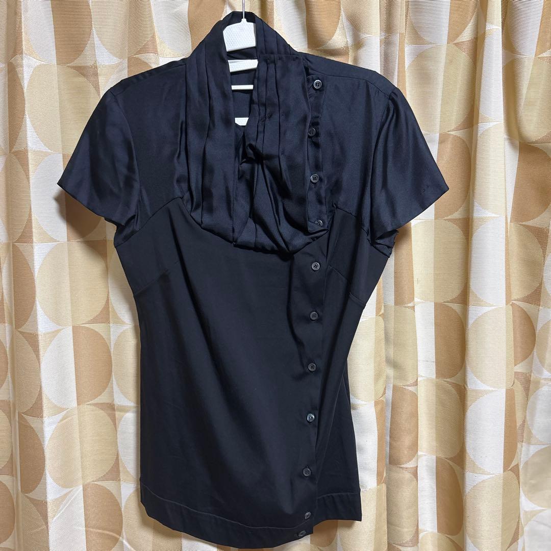 Black silk short-sleeve women's blouse hanging on a hanger against patterned curtains.