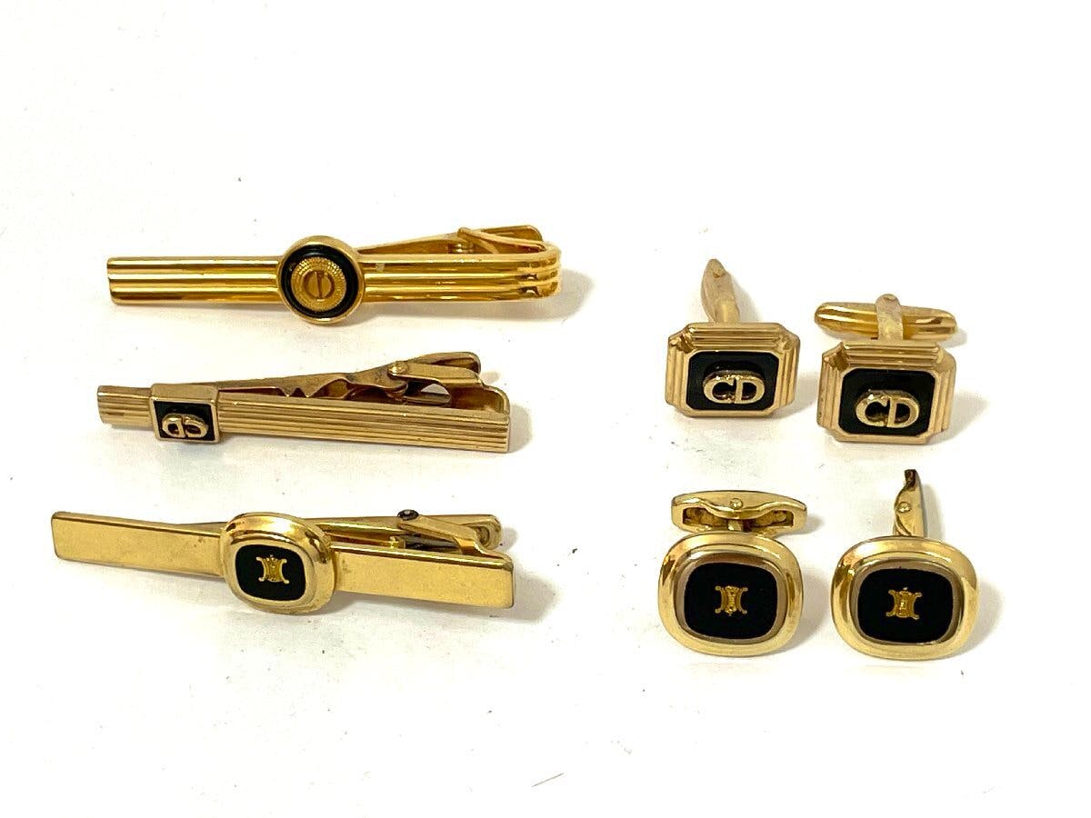 Gold-tone cufflinks and tie clips from CELINE and Dior arranged on a white background.