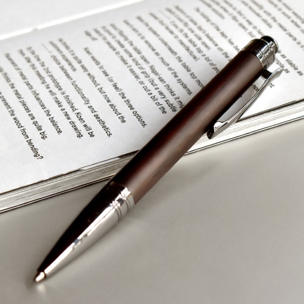 A premium ebony wooden ballpoint knock pen resting on an open book.