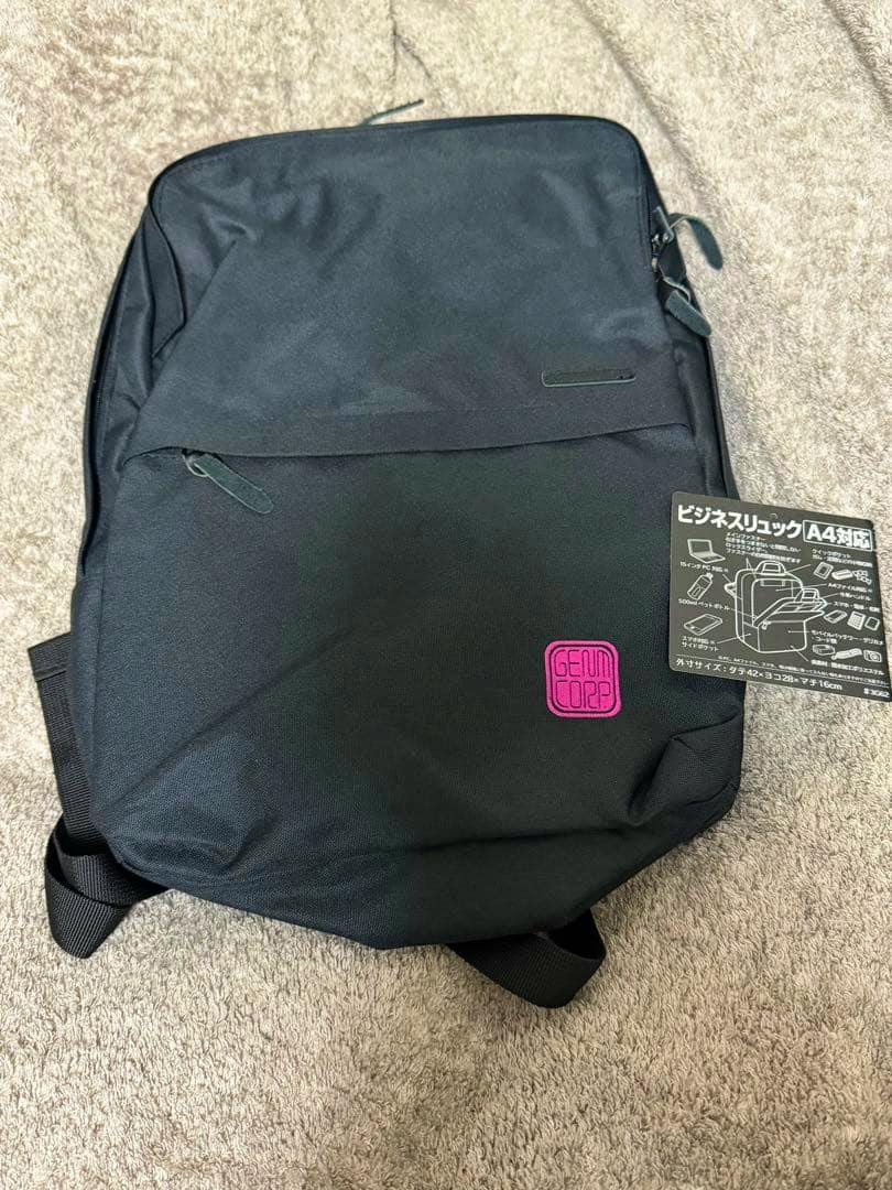 Front view of a black business backpack showing a small pink square patch and an attached product information tag.
