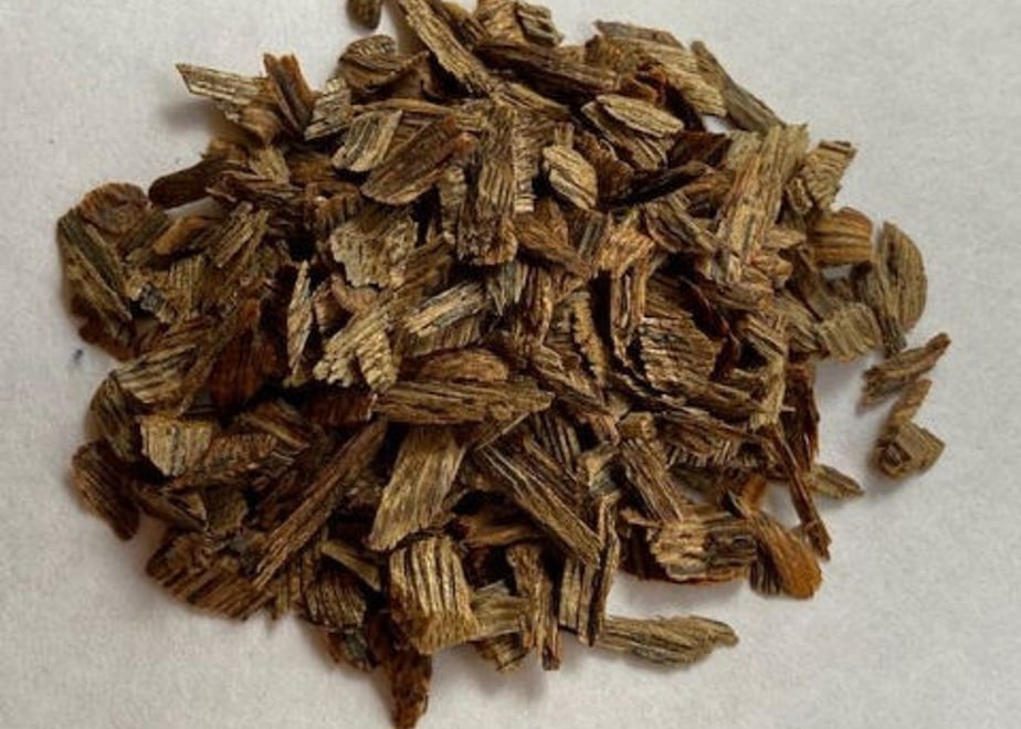 Close-up pile of shredded dark brown Kyara (aloeswood) incense chips on a white surface.