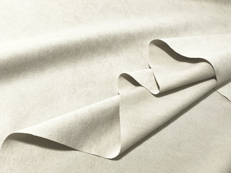 Light grayish-beige suede-like artificial leather fabric folded to show texture and drape.