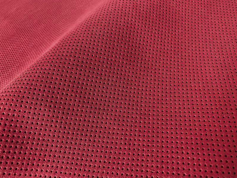 Close-up of deep red perforated suede-like artificial leather fabric showing small round holes and a darker backing.