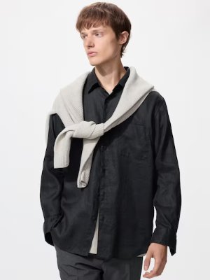A model wearing a black linen shirt with a light sweater draped over his shoulders.