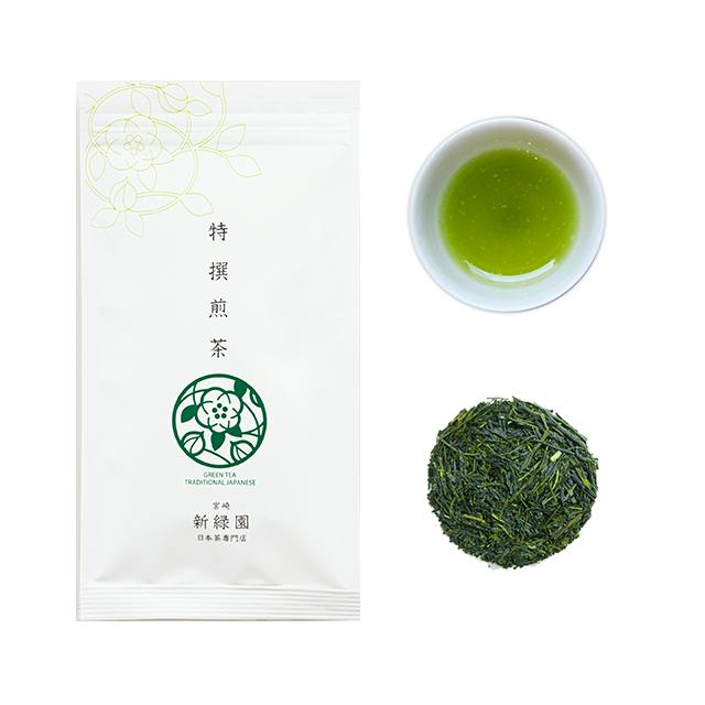 A white sealed pouch of green tea shown next to a cup of brewed green tea and a pile of loose green tea leaves.