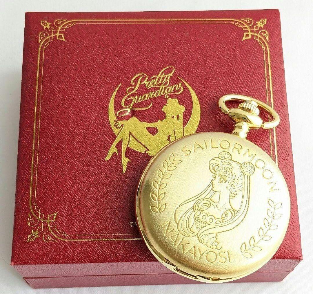 Gold Sailor Moon pocket watch with engraved cover resting on a red presentation box.