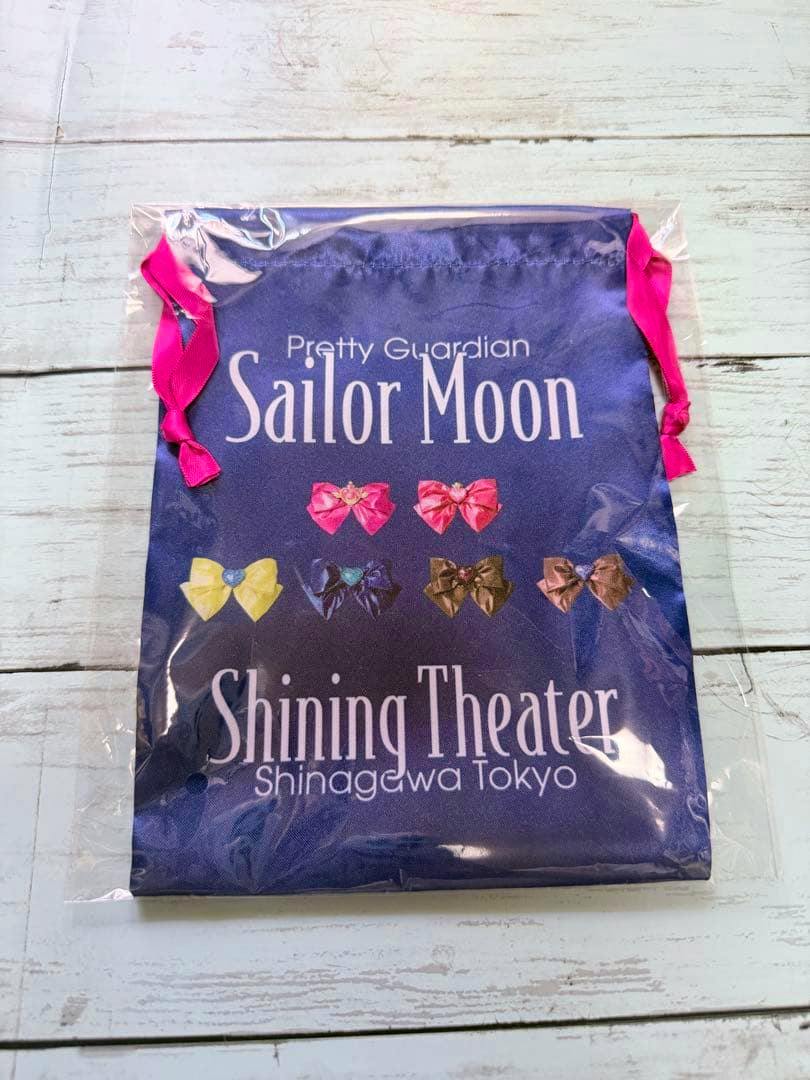 Front of a navy polyester Sailor Moon Shining Theater drawstring pouch with pink ribbons and printed bows, shown in clear plastic packaging.