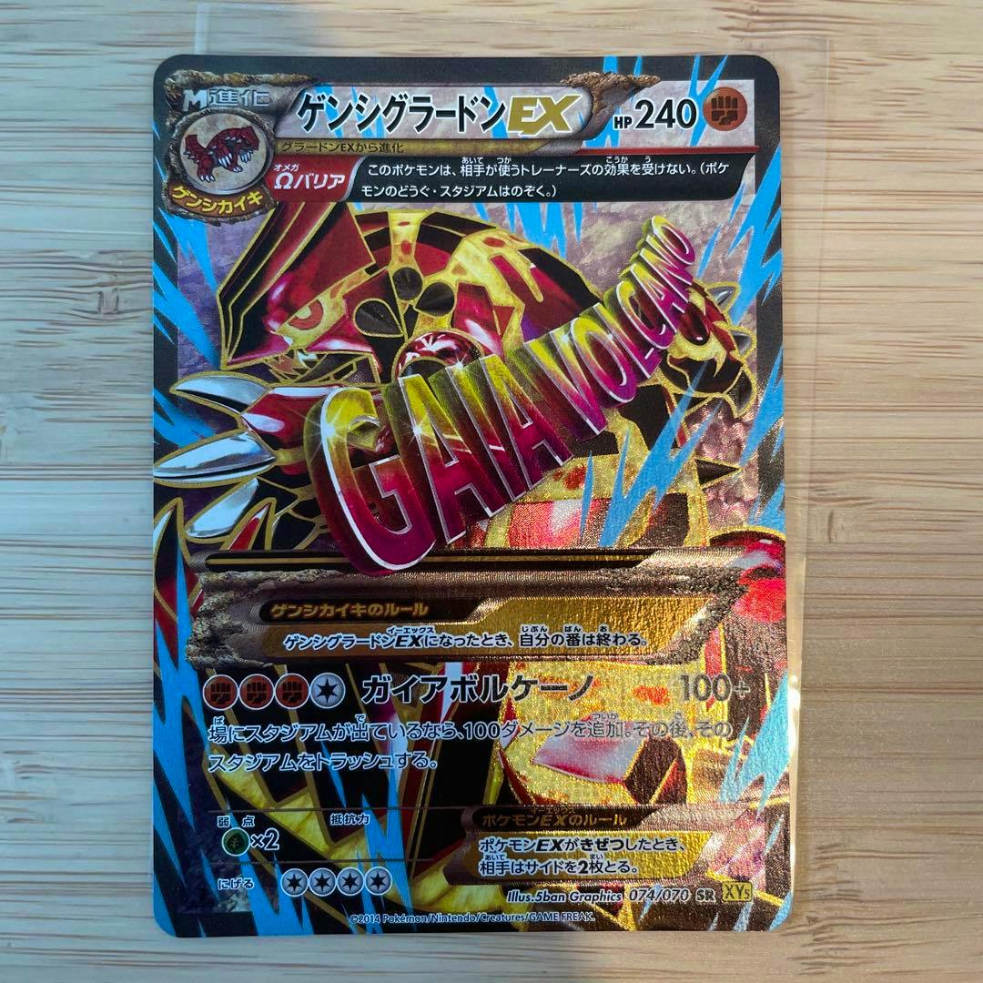 Photograph of the front of the trading card ゲンシグラードンEX SR XY5 ガイアボルケーノ 074/070 placed on a wooden surface.