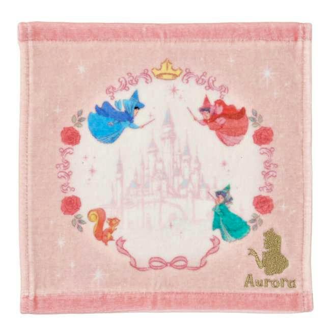 Square pink mini cotton towel showing a faint castle in the center, three fairies and roses around the border, and a gold 'Aurora' silhouette with text at the lower right.