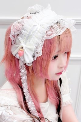A person wearing a white frilly lace headband with ribbon and a small strawberry ornament.