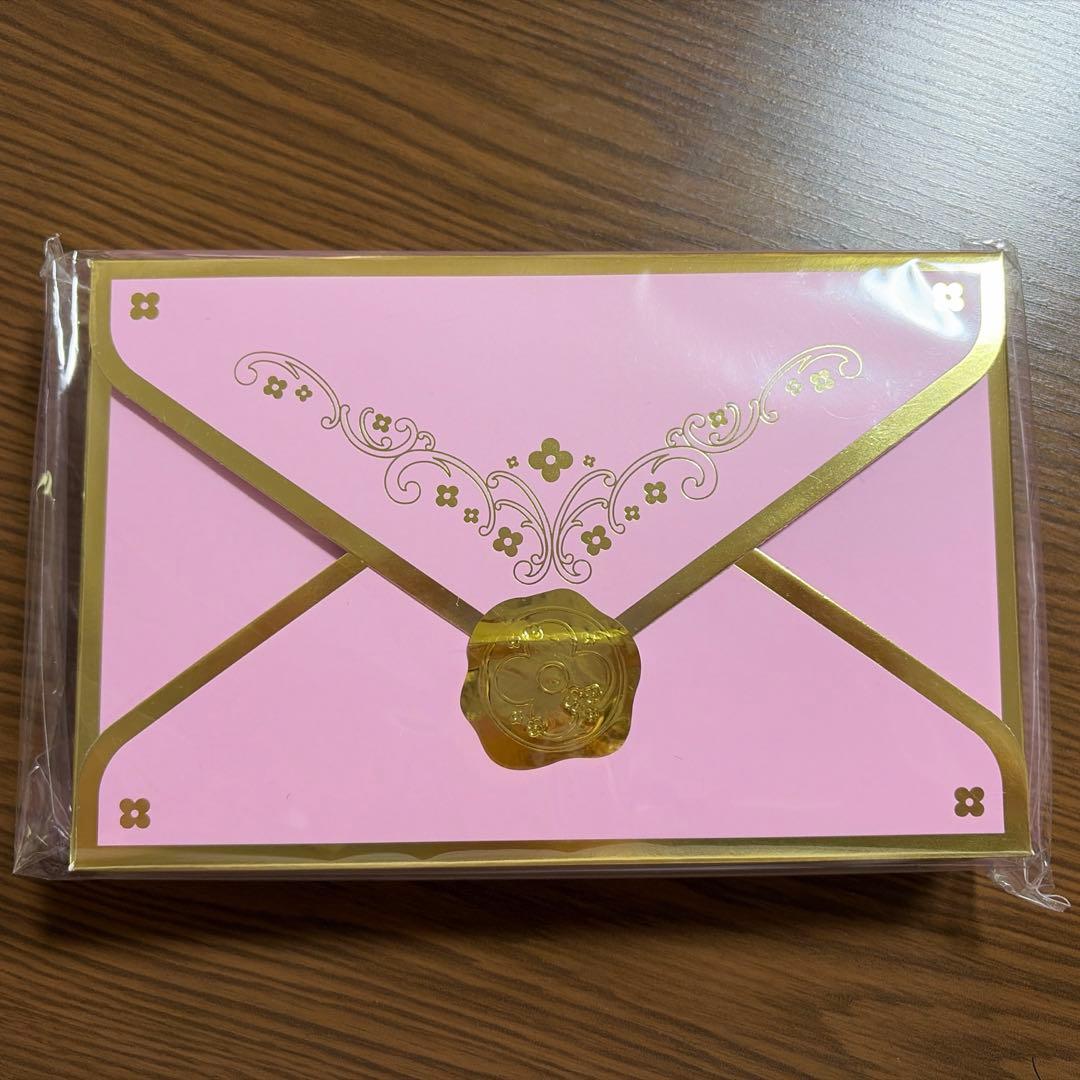 Sealed pink letter set with gold decorative borders and a gold seal design on a wooden surface.