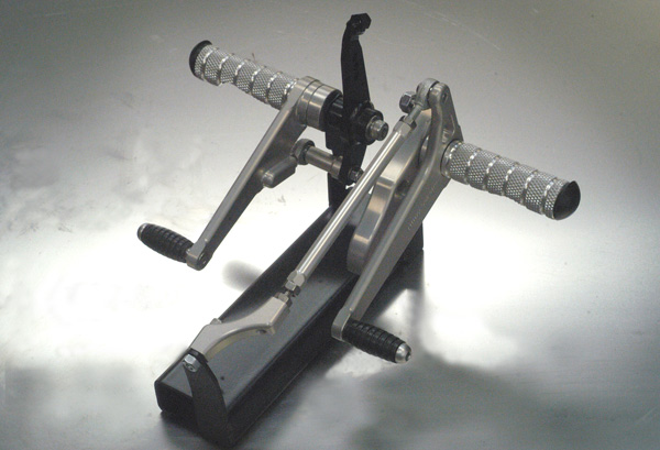 BMW motorcycle footpegs (Proper Step) showing silver pegs and mounting brackets on a reflective surface.
