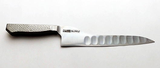 A chef knife laid on a white background, showing a textured handle and a stainless steel blade with hollowed grooves.
