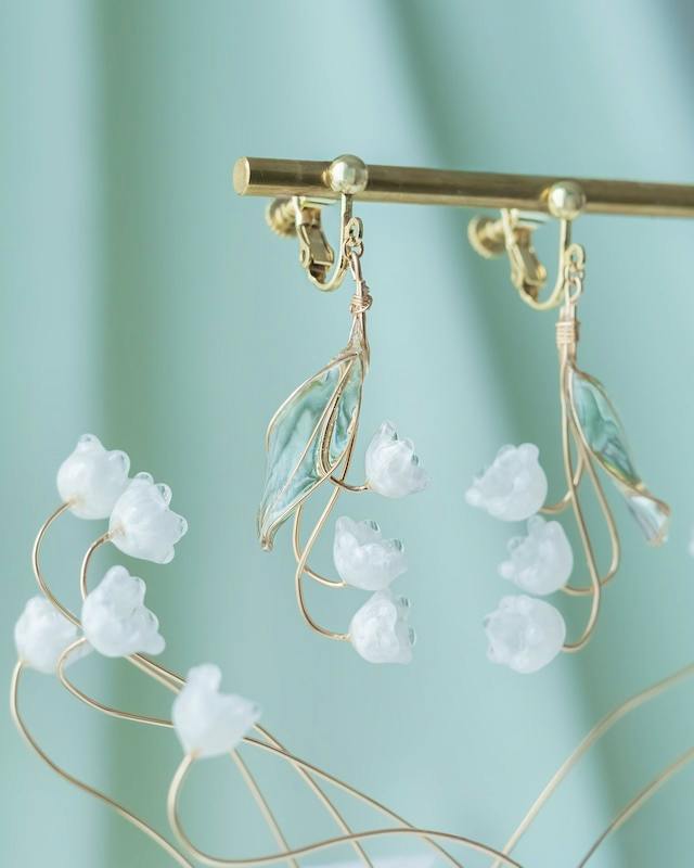 Pair of dangling earrings with small white flower beads and pale green leaf accents hanging from a display bar.