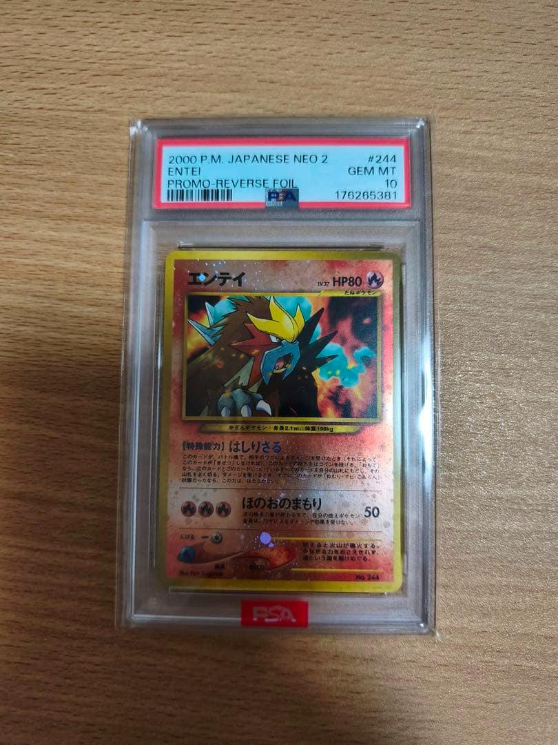 Front of a PSA-graded Entei Pokémon trading card in a clear PSA slab placed on a wooden surface.
